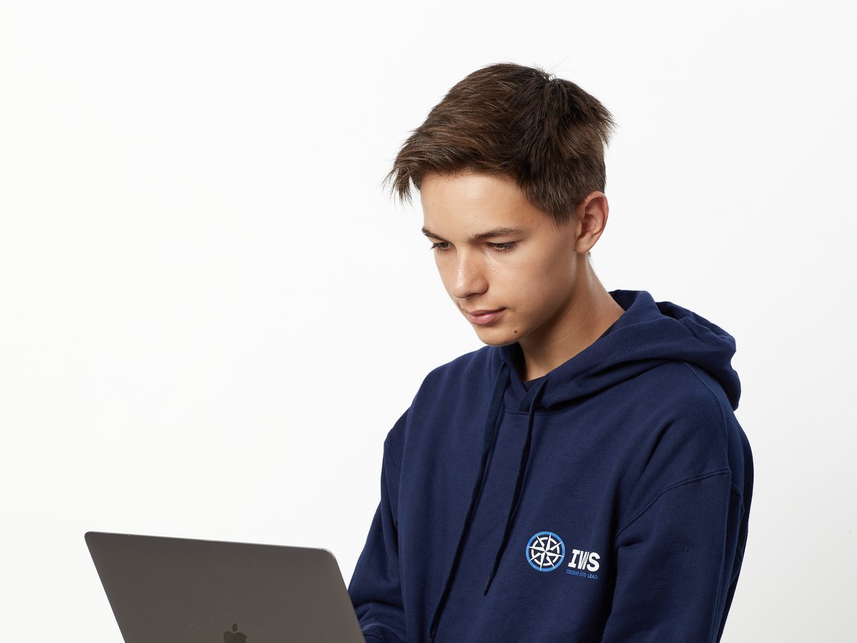 An IWS A Level student in a navy school hoodie, looking down at the open laptop he holds
