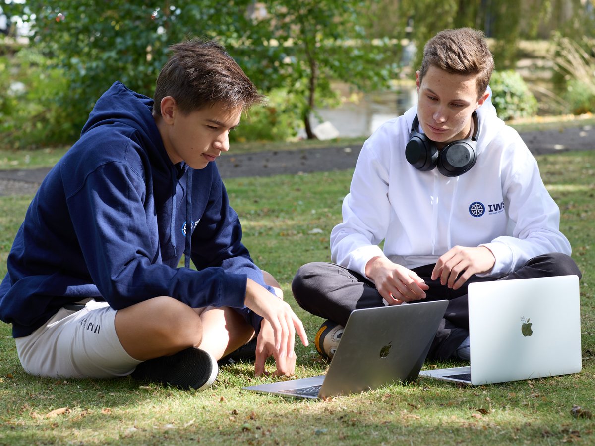 Two IWS students sitting on the grass in a park, each with an open laptop