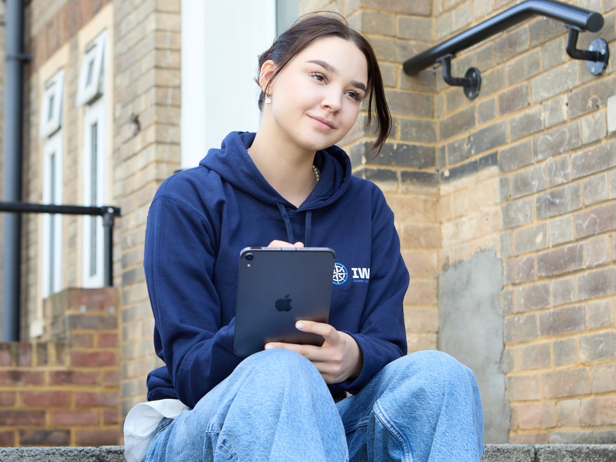 A student in an IWS hoodie sitting with a tablet in her hands, looking up with a calm smile