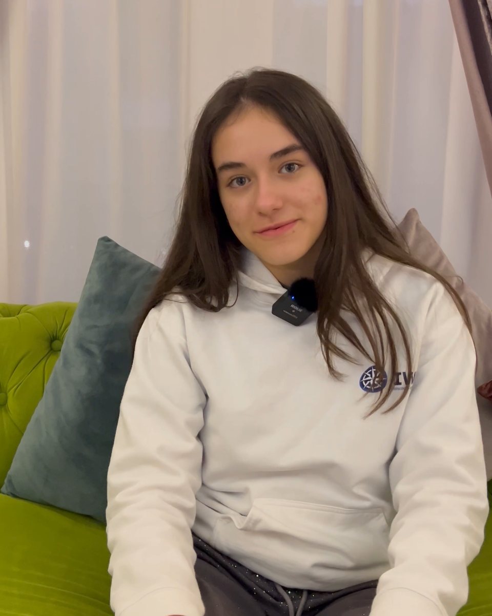 A student in an IWS hoodie smiling to the camera, sitting at home