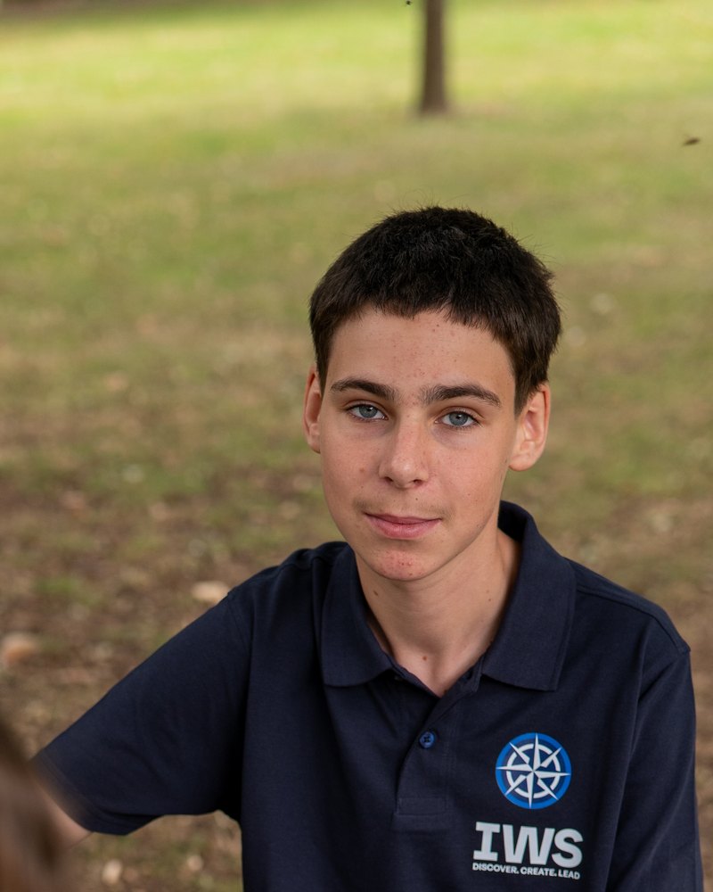 An IWS student in a navy polo looking straight at the camera across a table in a park