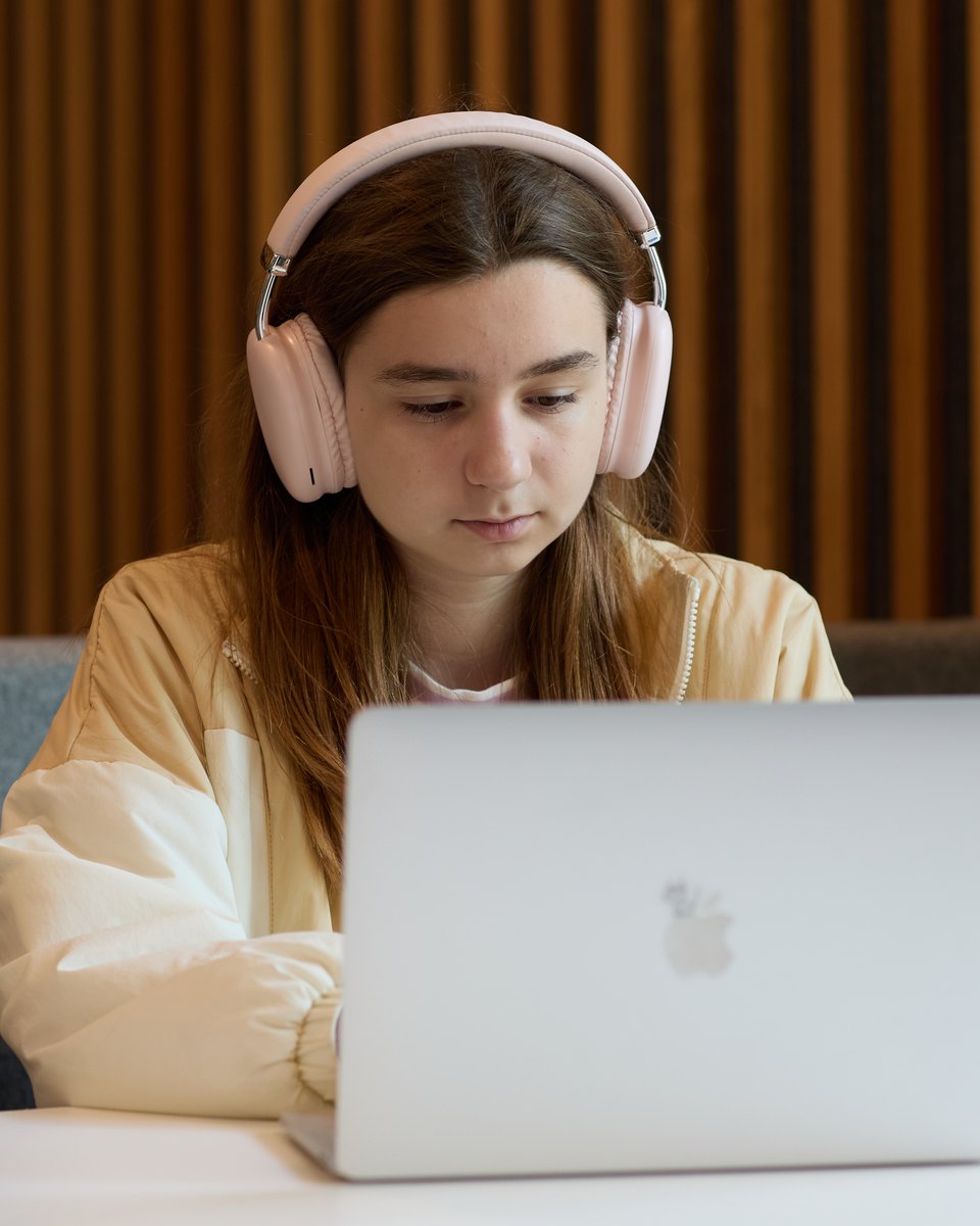 An IWS Primary student in pink headphones, working at her laptop at a white table