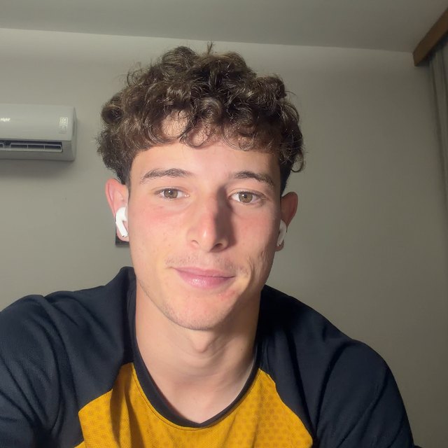 Adrian E., with curly hair and a white earbud, smiling a little at the camera