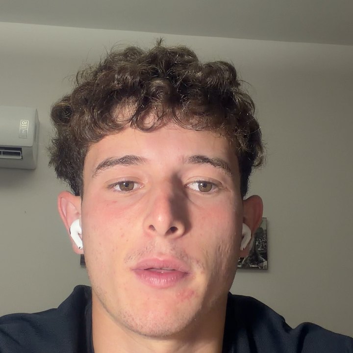 Adrian E., with a white earbud in, speaking to the camera in a quiet room
