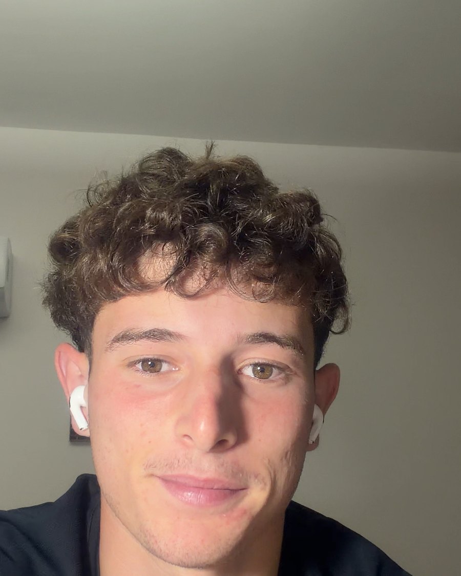 Adrian E., with curly hair and a white earbud, smiling a little at the camera