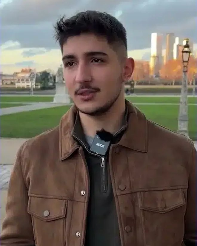 Aydın T., an IWS alumnus, standing in a park at sunset in a brown suede jacket, with golden towers behind him