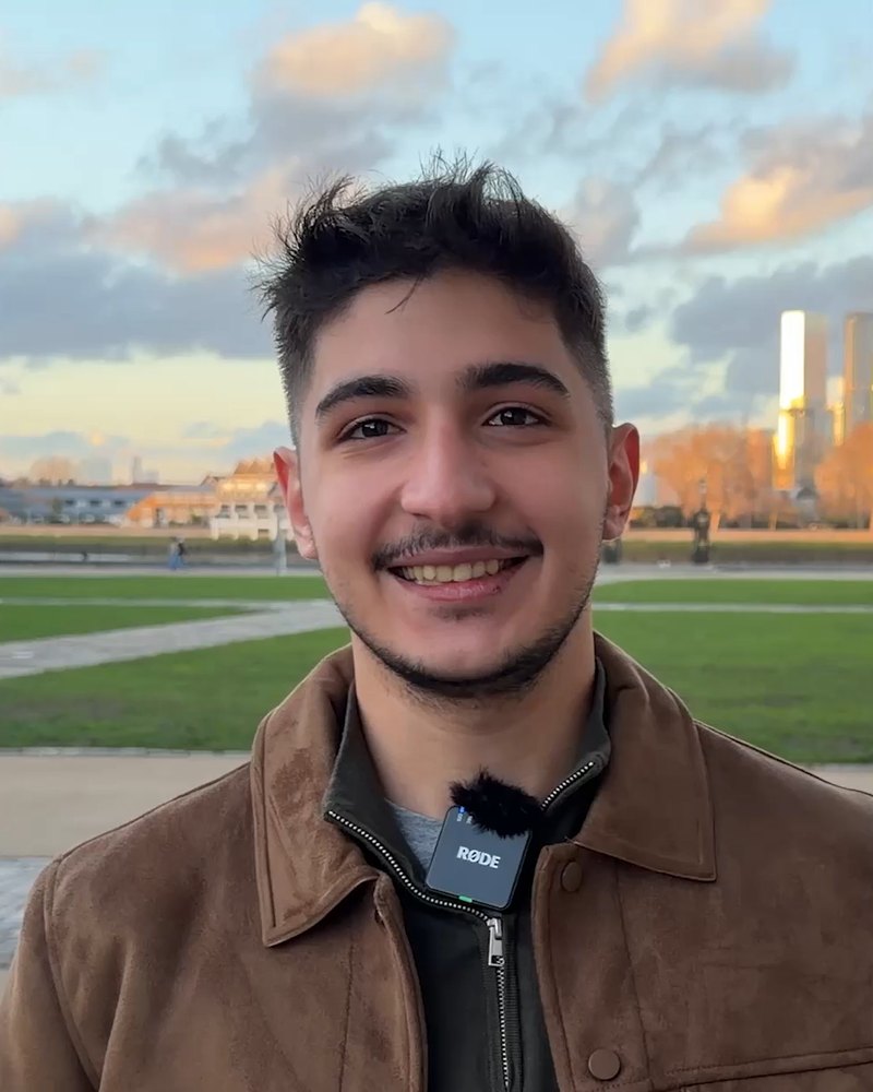 Aydın T., smiling, in a brown suede jacket on a park lawn at sunset