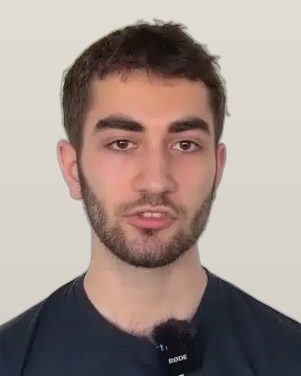 Emre K., an IWS alumnus with a short beard, speaking to camera in a dark T-shirt