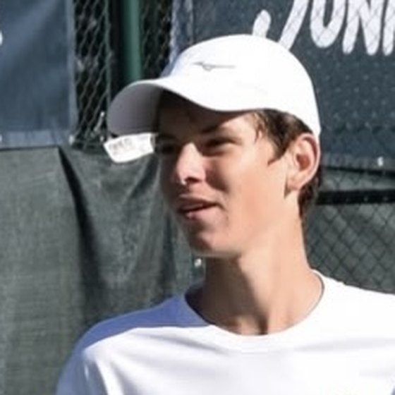 Georgiy G. on a tennis court in a white cap and T-shirt, a racket in his hand