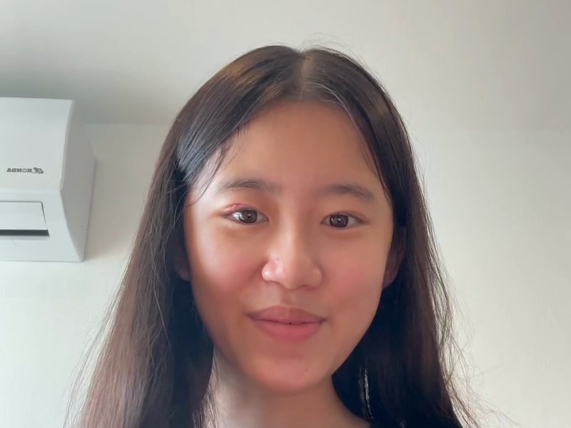 Kei Y., close to the camera, with long dark hair, in front of a white wall