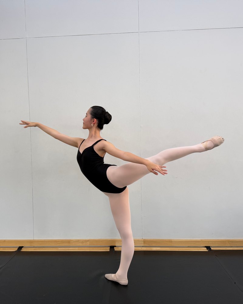 Kei Y. holding a ballet arabesque in front of a white studio wall