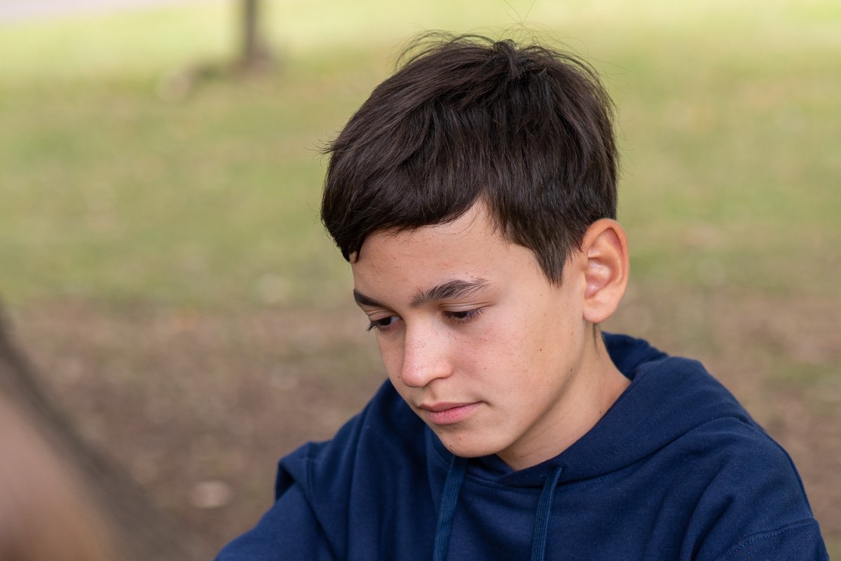 An IWS student in a navy hoodie looking down in concentration, outdoors in a park