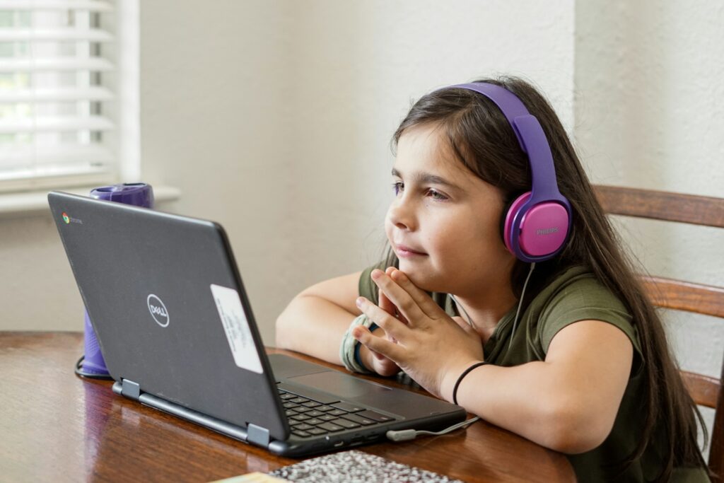 A young primary-age child learning online with headphones on a laptop — IWS Online School